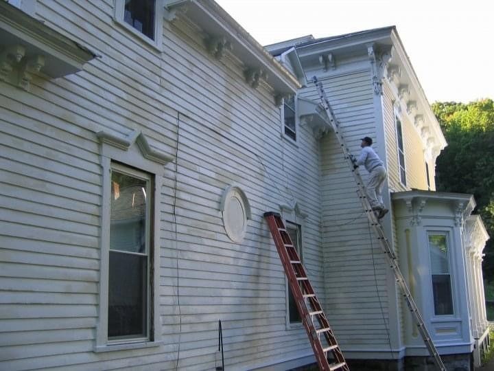 Two workers on ladders painting a white house exterior