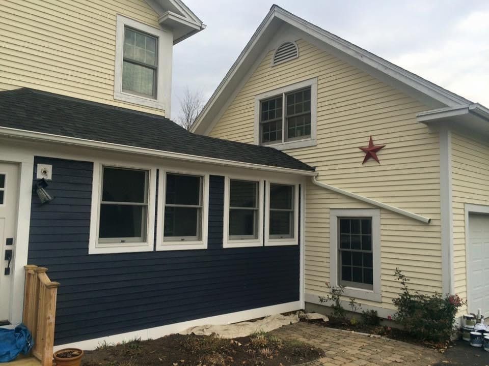 Side of a beige house with dark blue lower siding, white trim windows, and a red star decoration.