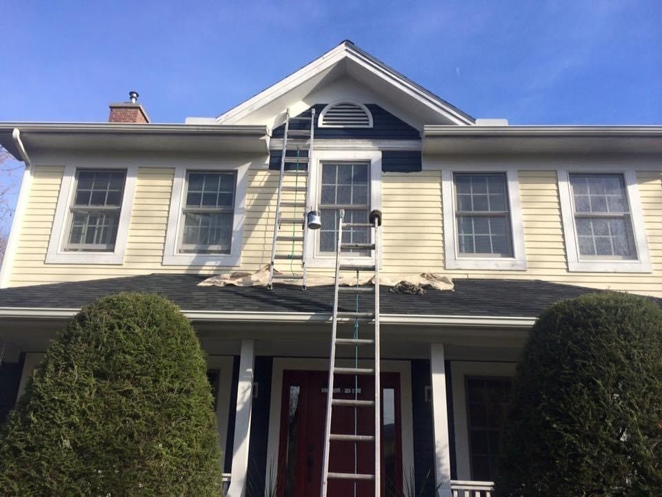 Yellow house exterior with a ladder leaning to a second-floor window between two trimmed bushes