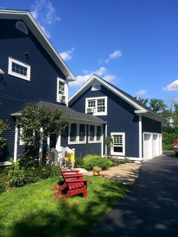Blue house with white trim, front porch, red chairs, and a driveway under a sunny sky