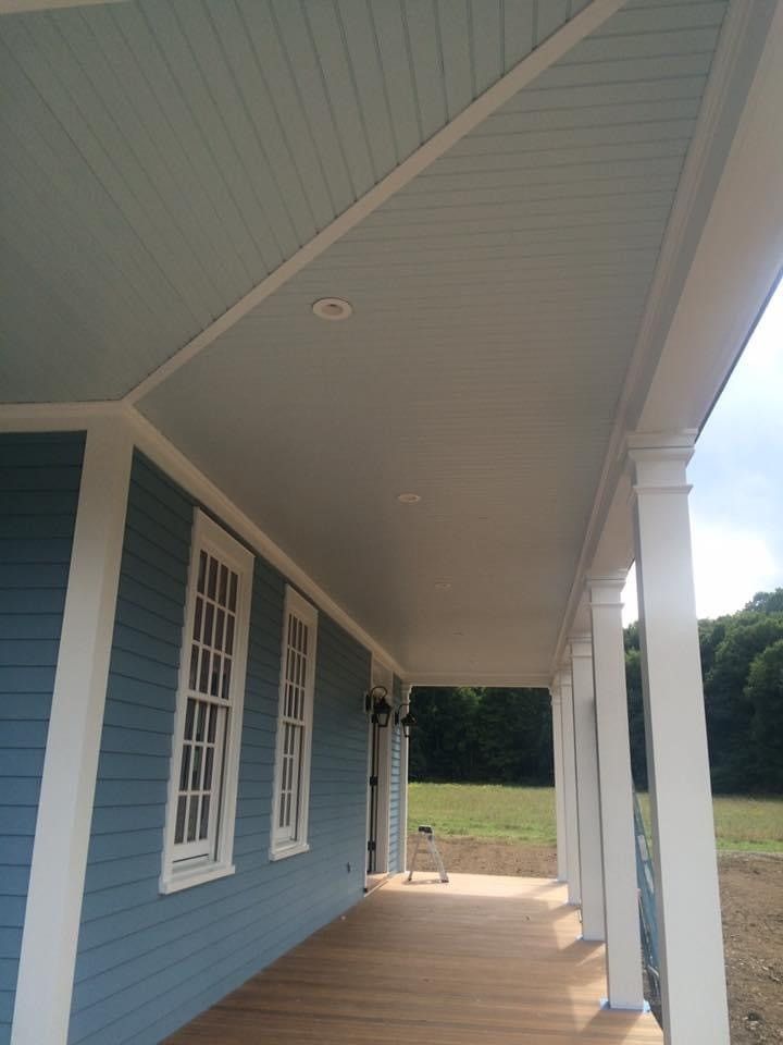 Blue house porch with white trim and columns, overlooking a grassy yard under a covered roof