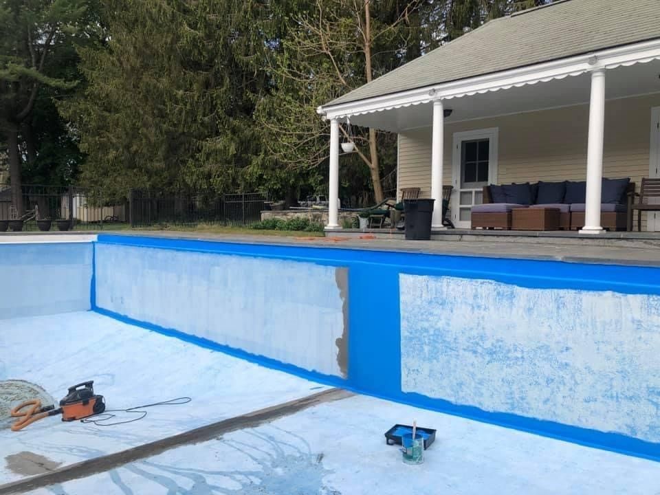 Empty swimming pool being painted blue and white beside a covered patio