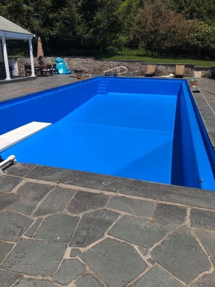 Bright blue empty swimming pool beside a stone patio and grassy yard