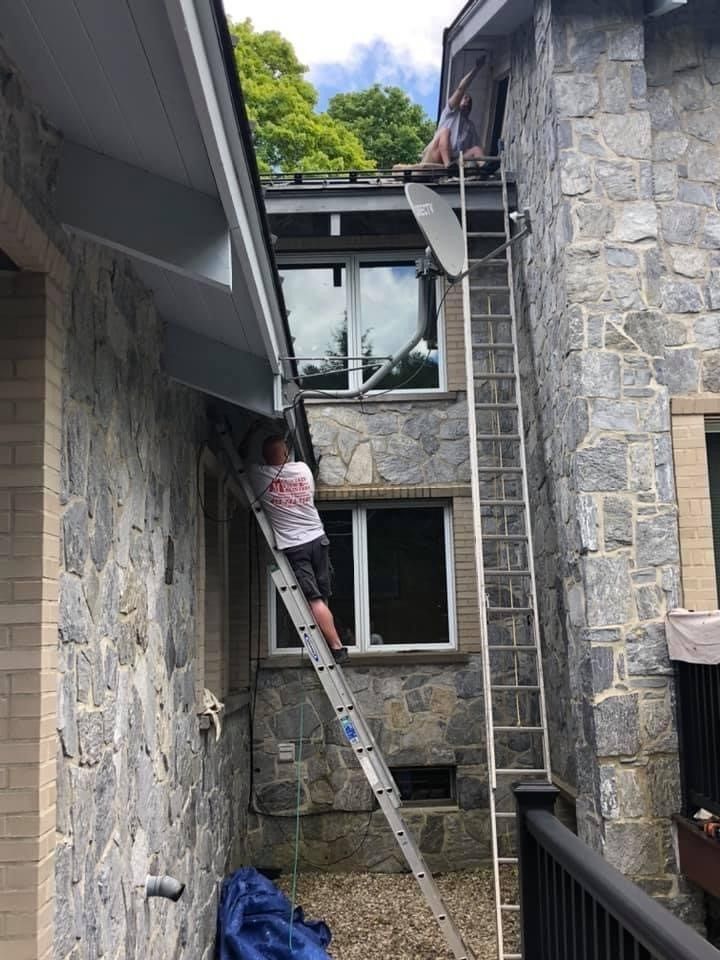 Person on ladder cleaning or working on a window between two stone buildings.