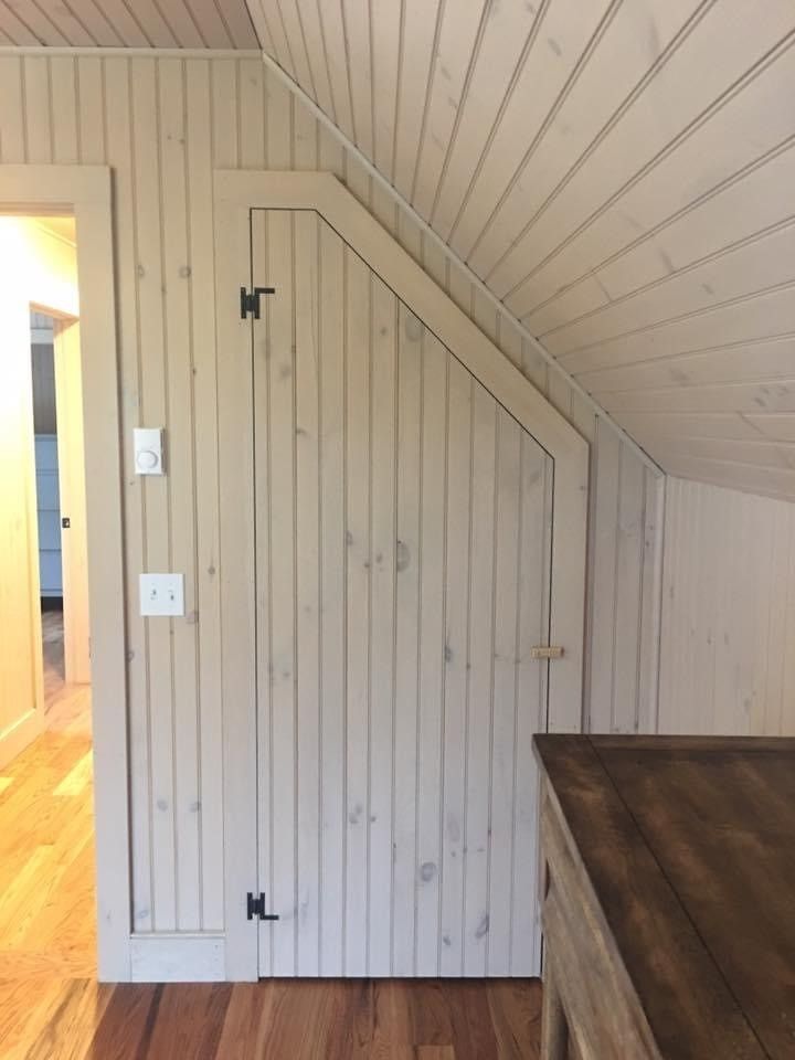 Small white paneled door in a sloped ceiling hallway beside a wooden table and open doorway