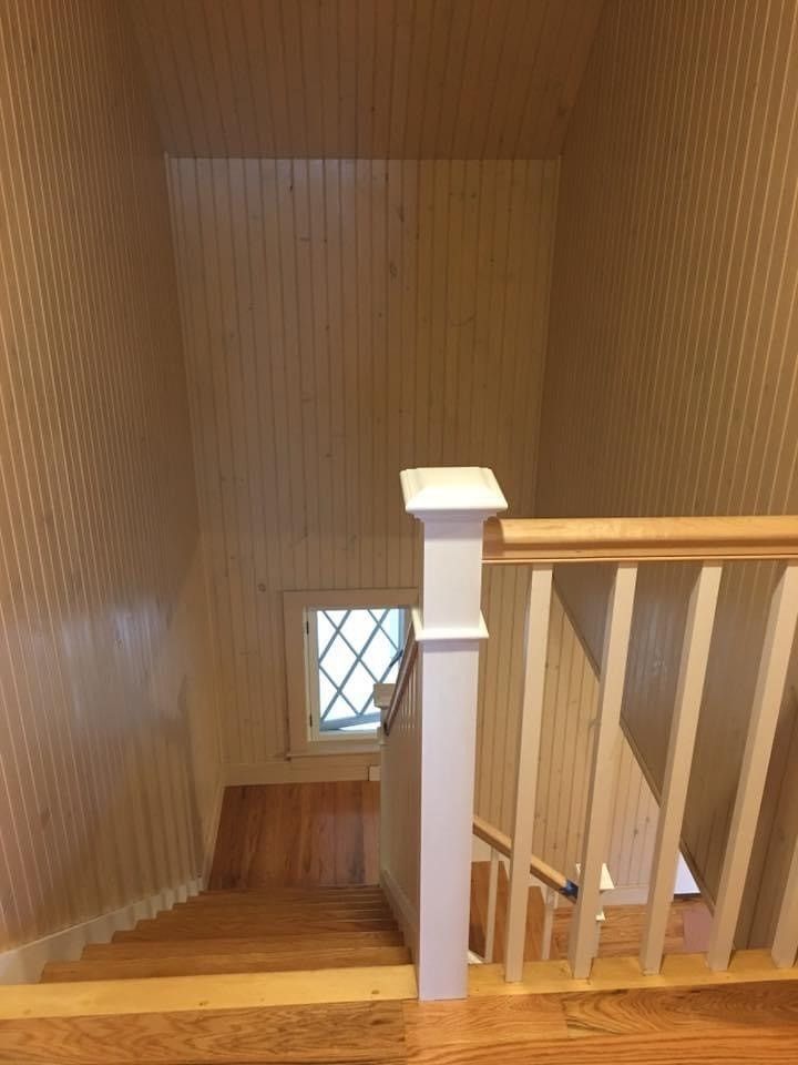 Staircase with wood-paneled walls, white railing, and a small window at the landing.