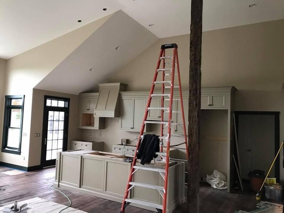 Renovated kitchen with red ladder, white cabinets, vaulted ceiling, and exposed wood beam