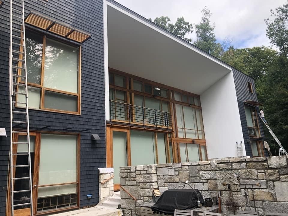 Modern two-story house with dark wood siding, large windows, and a stone patio wall outdoors