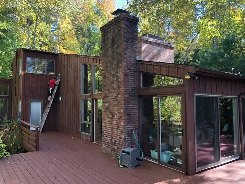 Modern wood-and-brick house exterior with large windows, deck, and surrounding trees