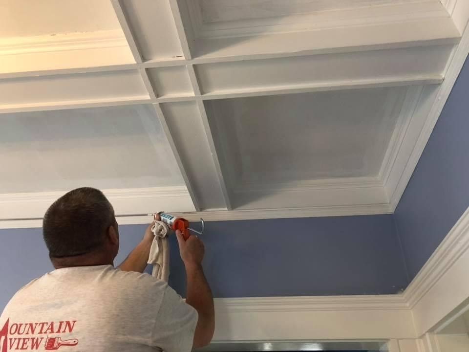 Worker painting a blue coffered ceiling with a spray gun