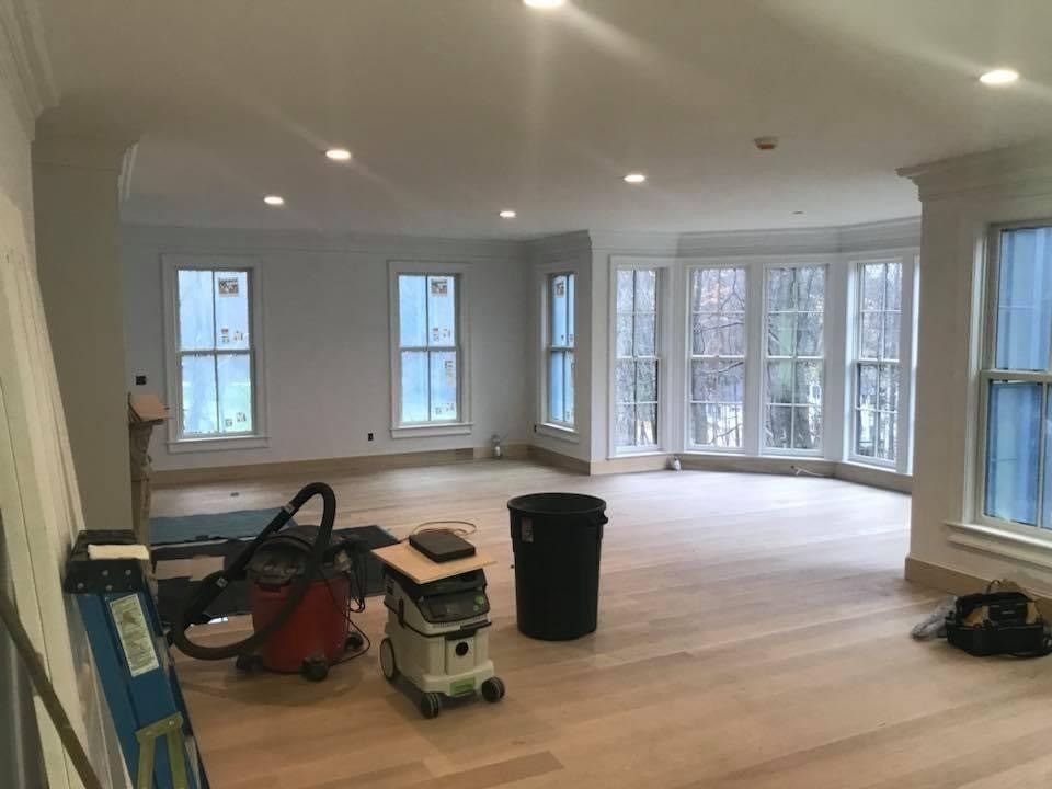 Large empty living room with recessed lights, wide windows, and cleaning equipment on the floor