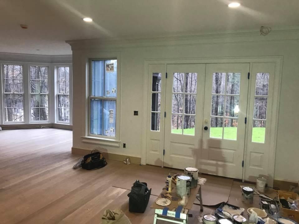 Bright empty room with wood floors, large windows, and a white double glass door; renovation items on the floor