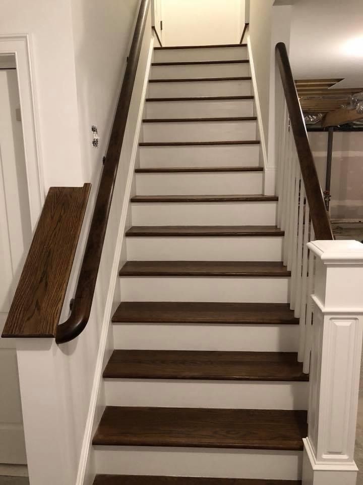 Narrow indoor staircase with white walls, dark treads, and wooden handrails