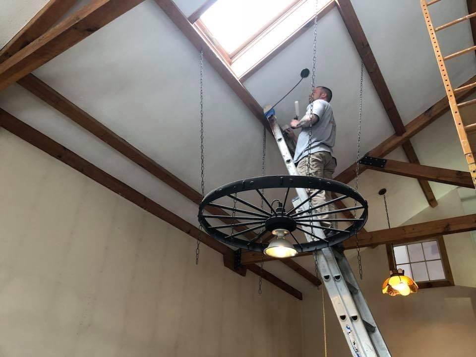 Worker on a suspended circular lift installing a skylight in a wood-beamed ceiling.