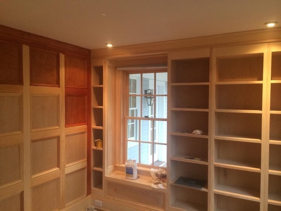 Built-in wooden bookshelves and cabinets in a warmly lit room with a central window.