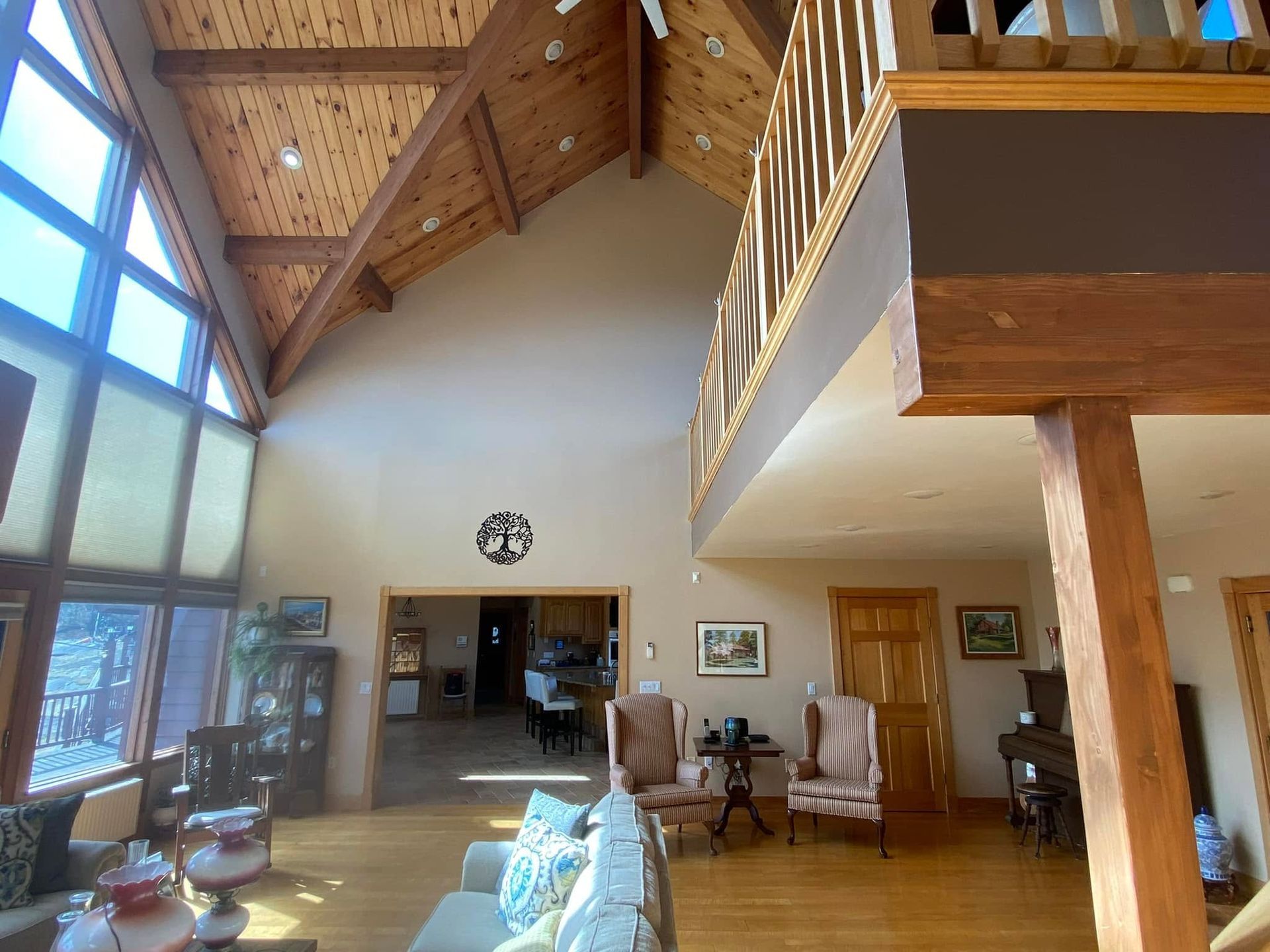 Spacious living room with high wood ceiling, large windows, and a balcony overlooking seating and a fireplace.
