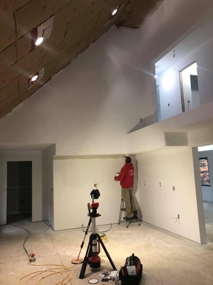 Two workers on ladders painting a high white interior wall in a large room under construction
