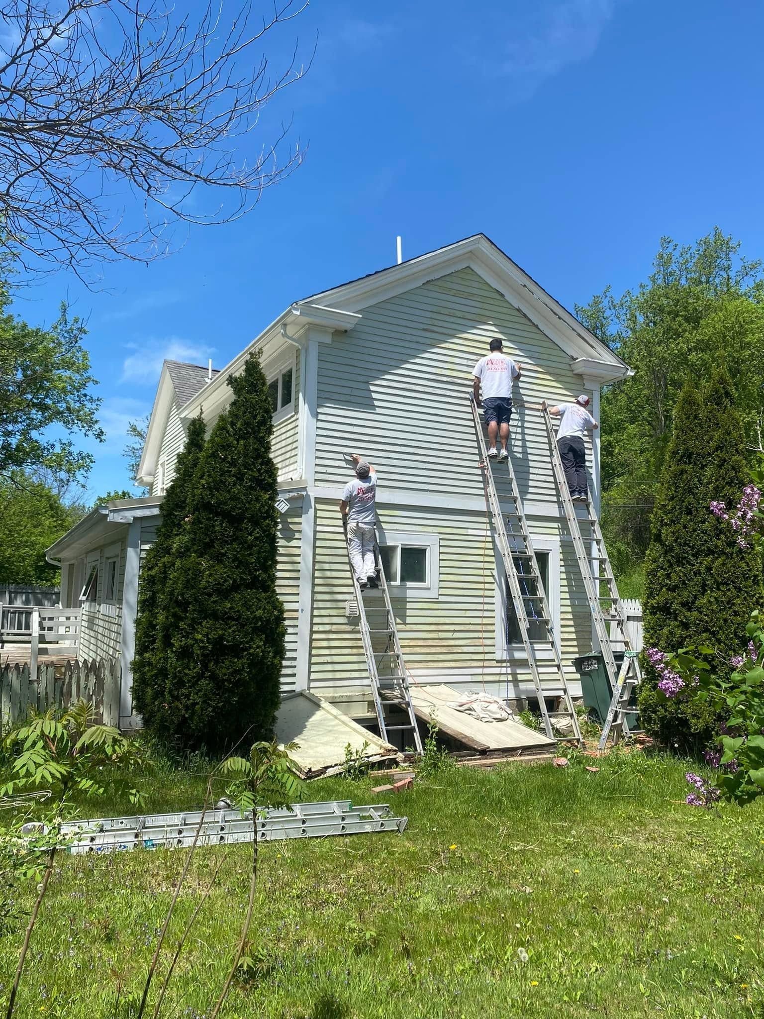 Two workers on ladders painting a white house exterior on a sunny day