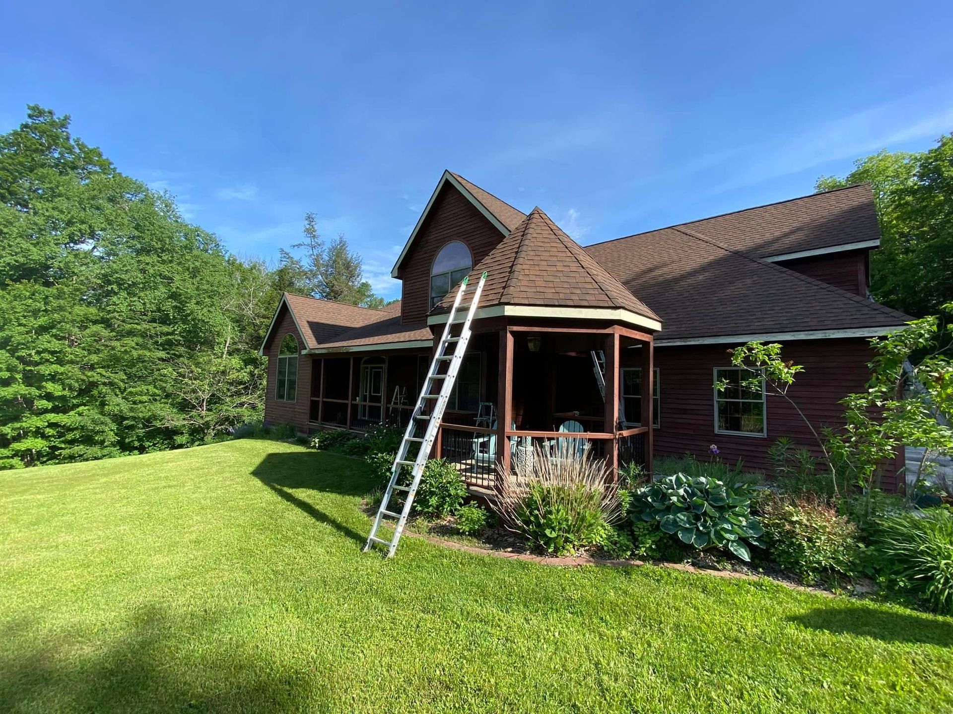 House with a ladder leaning against the front porch in a sunny green yard