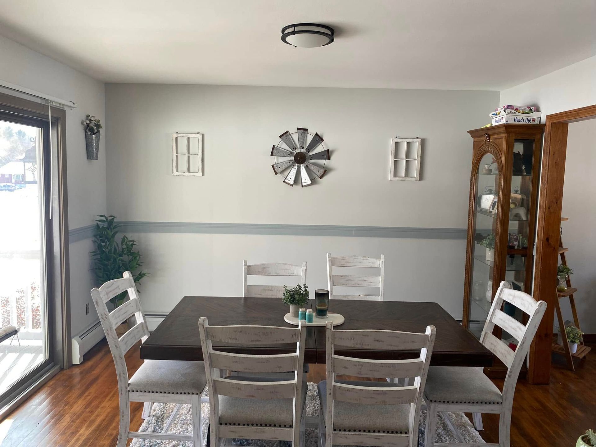 Dining room with dark table and white chairs, wall clock, sliding glass door, and wooden cabinet.