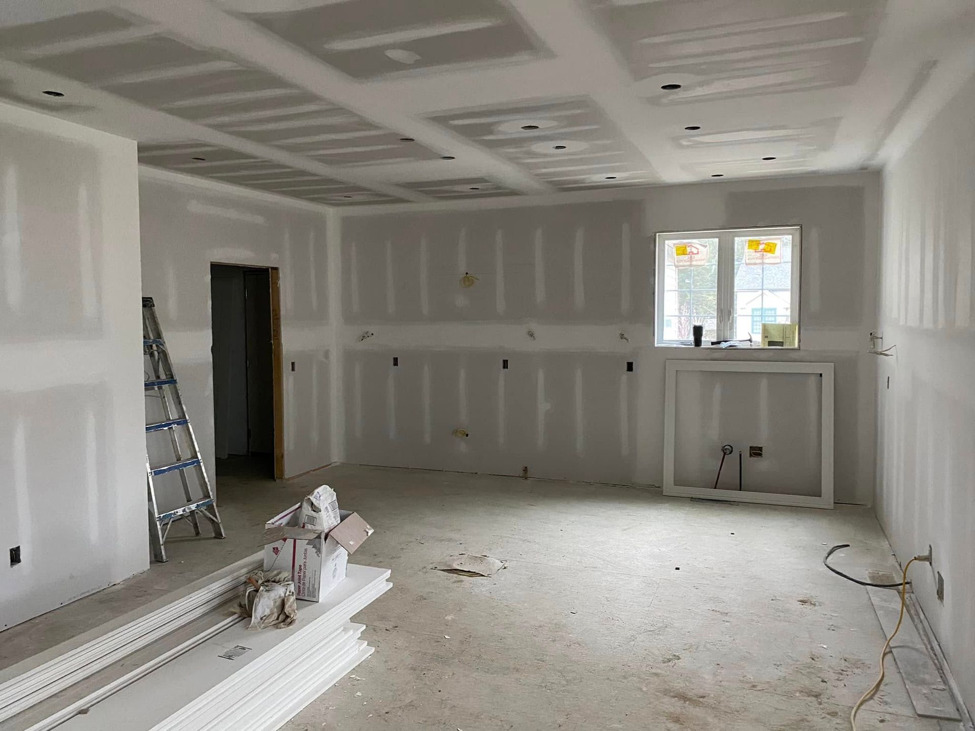 Partially finished room with drywall, window, ladder, and construction materials on the floor