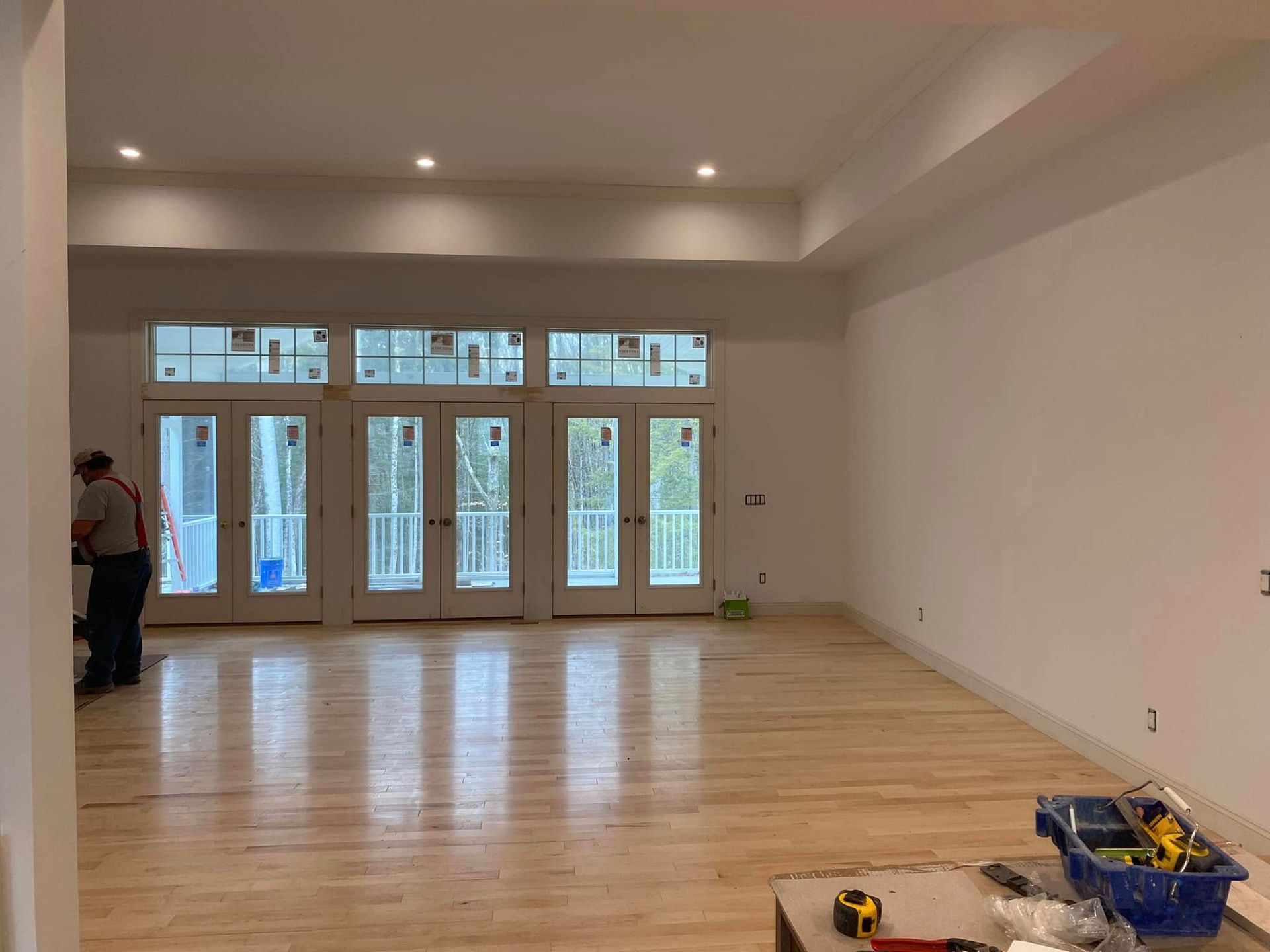 Empty room with light wood floors, white walls, French doors, and a worker on the left side.