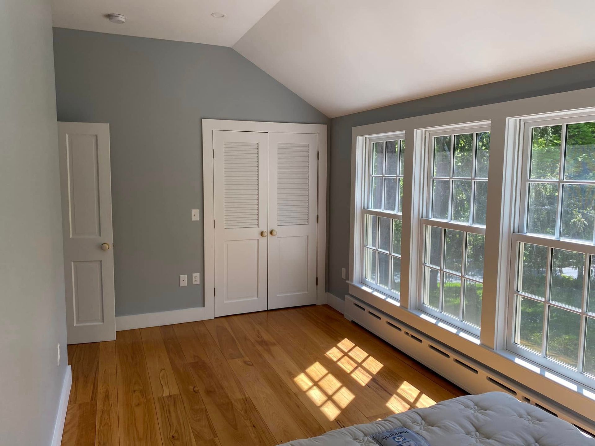 Empty sunlit bedroom with hardwood floors, gray walls, white closets, and large windows
