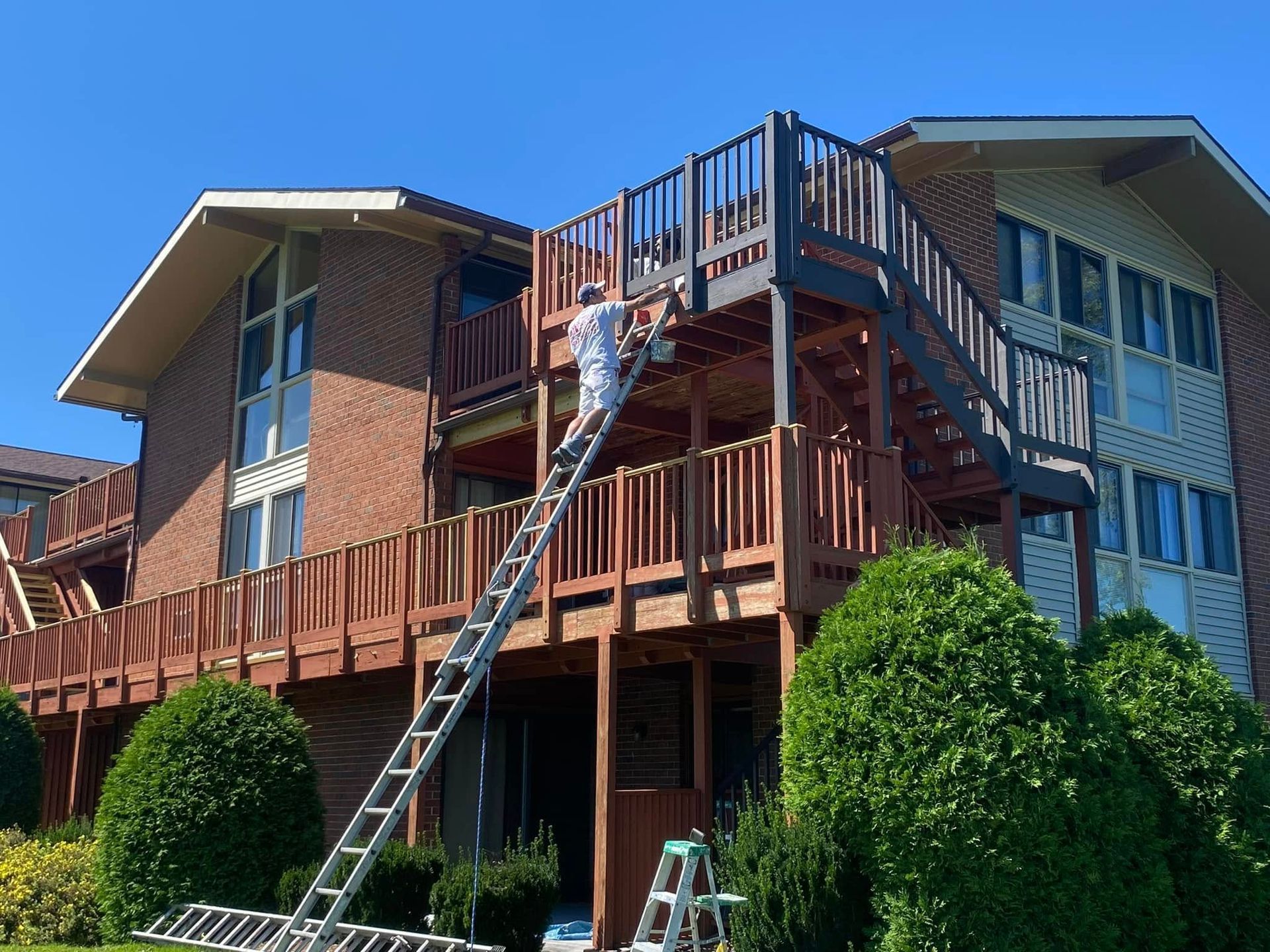 Person on a ladder repairing a wooden deck on a brick apartment building