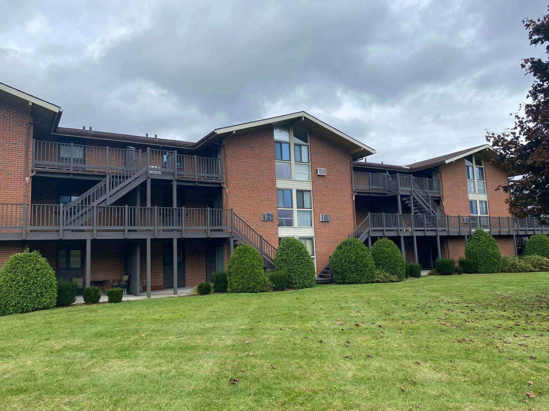Brick apartment building with dark wooden balconies and green lawn under cloudy sky