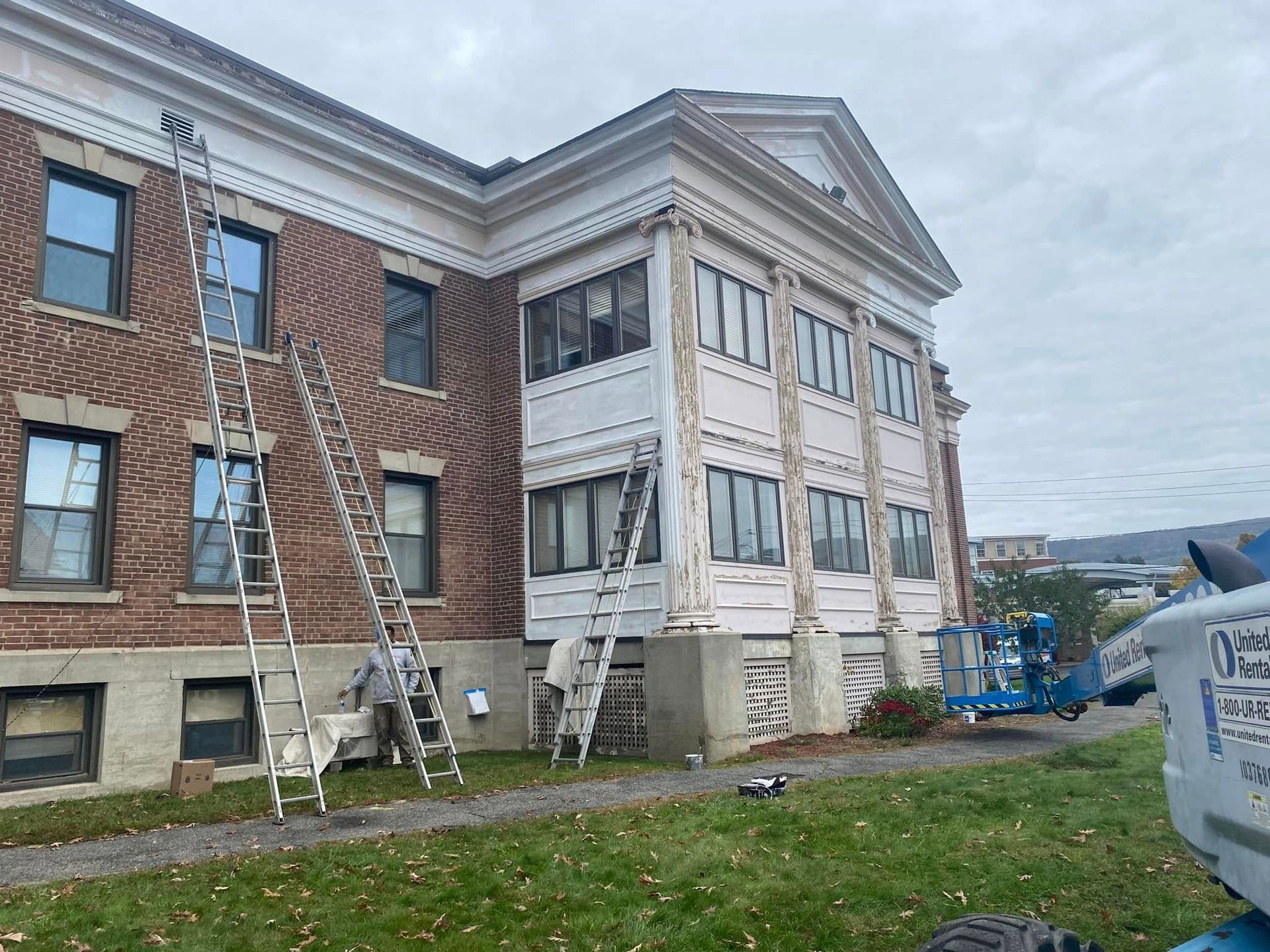 Brick school building with workers on ladders performing exterior repairs under a cloudy sky
