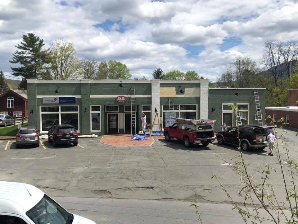 Small row of storefronts with parked cars and a cloudy sky above.