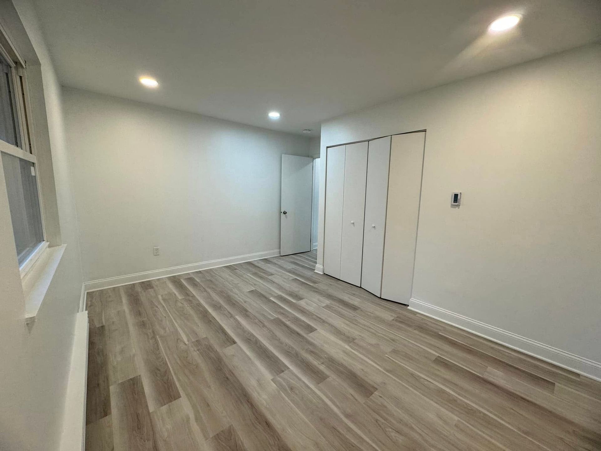 Empty modern room with gray walls, wood-look flooring, recessed lights, and white closet doors.