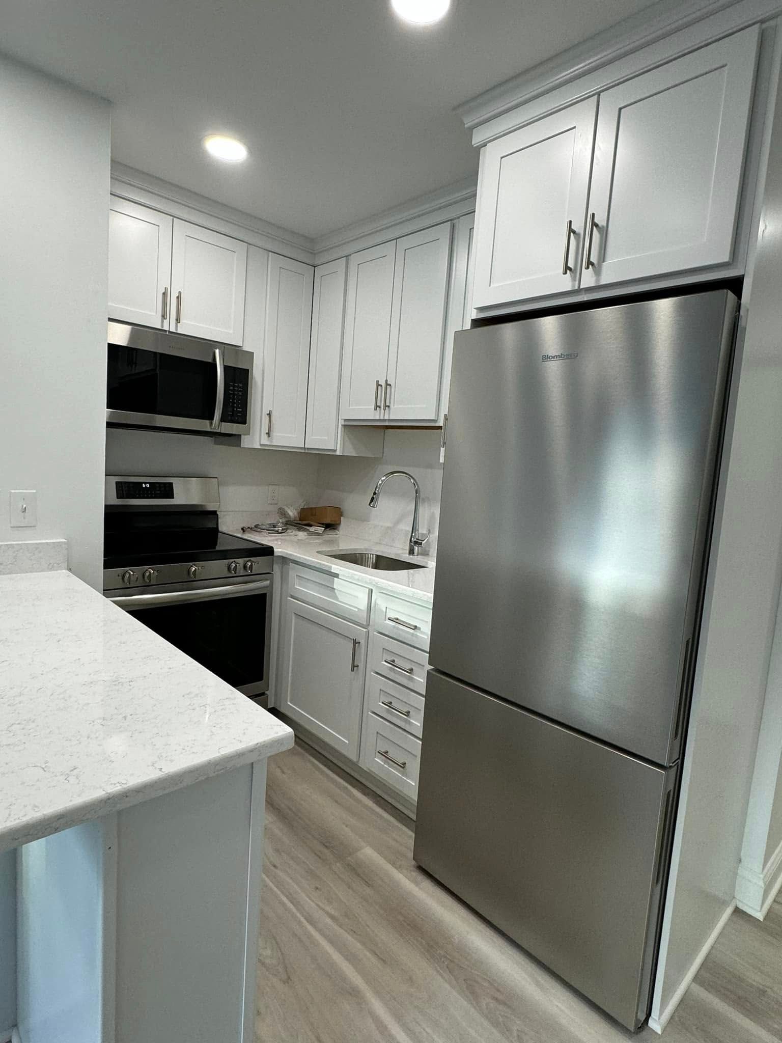 Bright white kitchen with stainless steel appliances, white cabinets, and a light wood floor