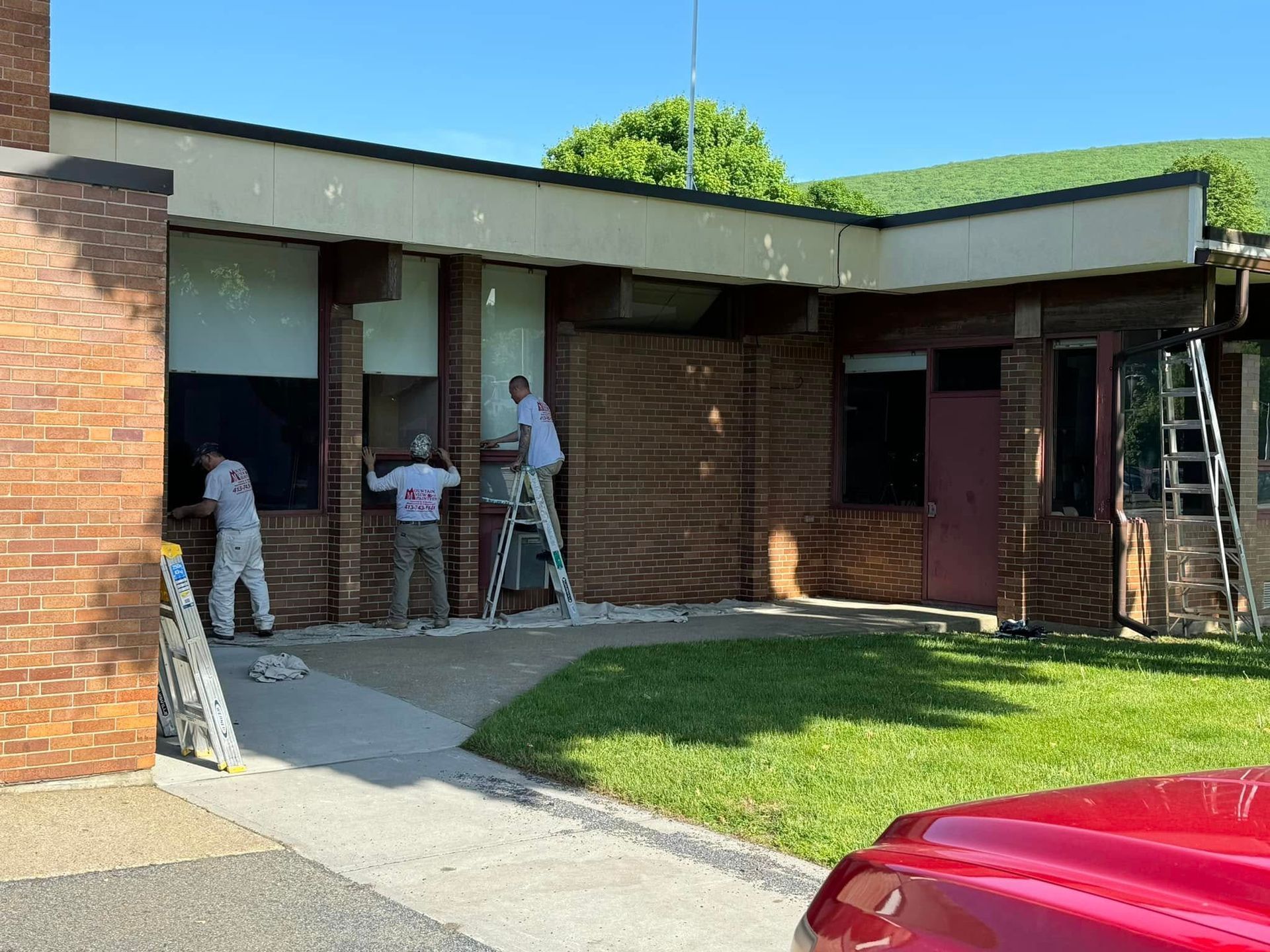 People working on a brick building exterior under a covered walkway, with ladders and tools.