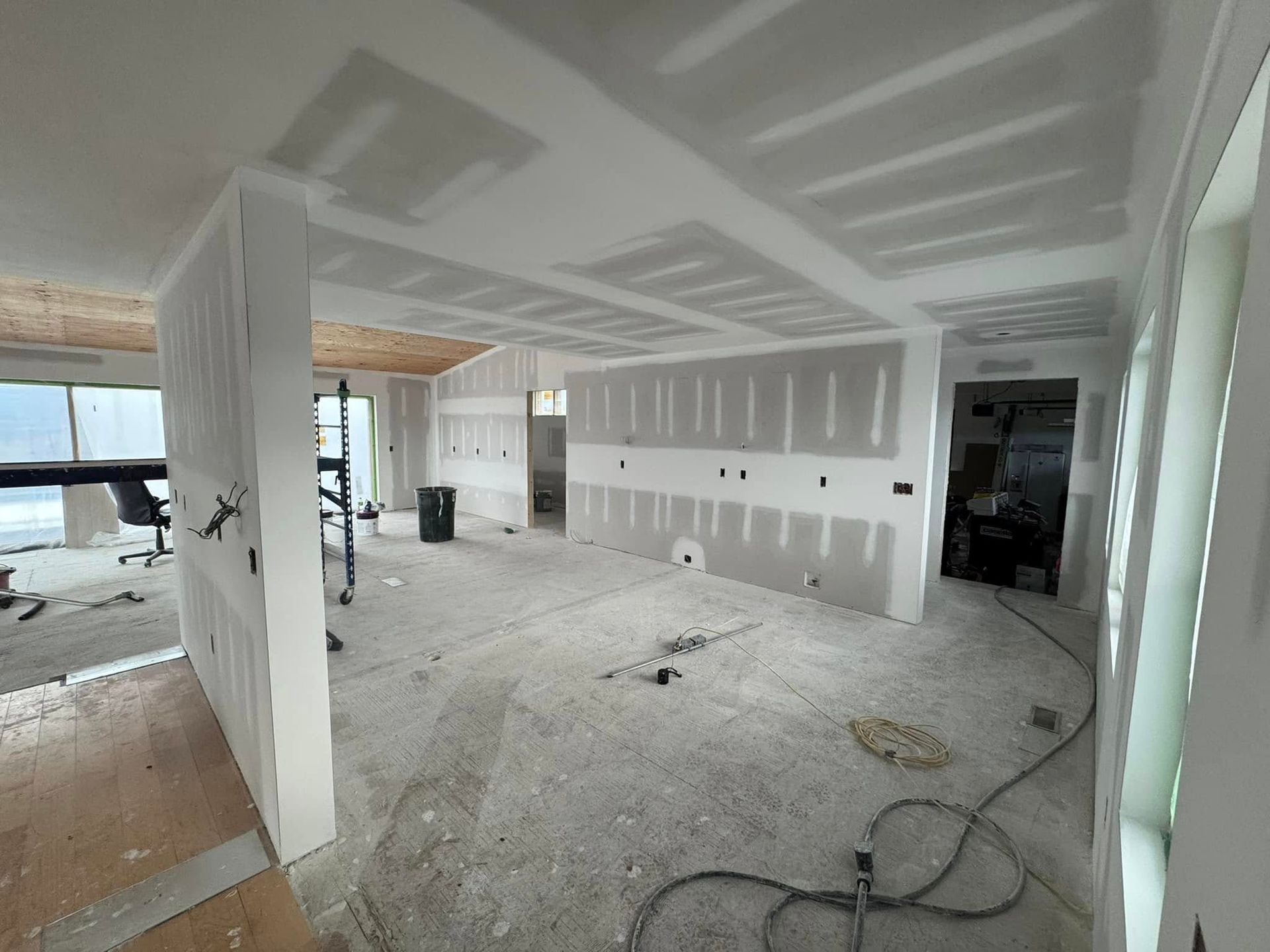 Renovated unfinished room with drywall, white walls, and construction materials scattered on the floor.