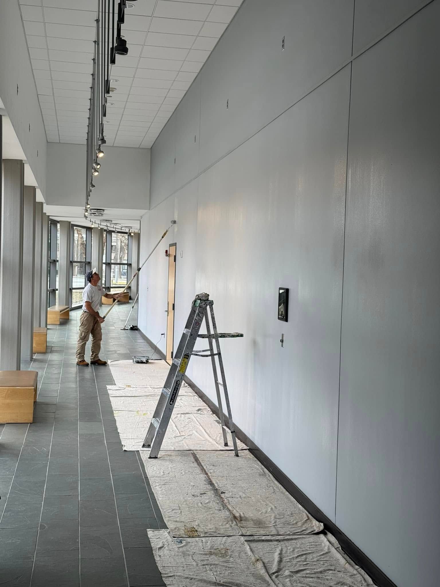 Long hallway under construction with ladder, tools, and workers near unfinished white walls