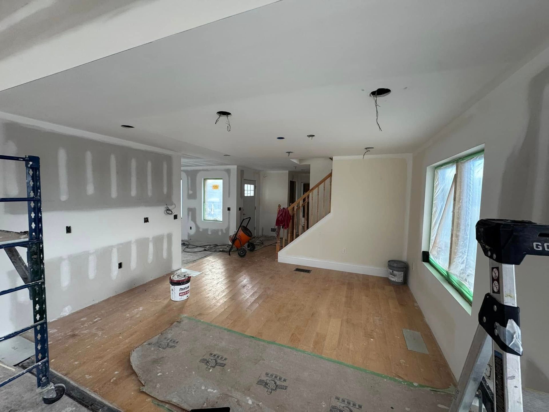 Unfinished living room with drywall, hardwood floor, windows, and a fireplace under renovation.