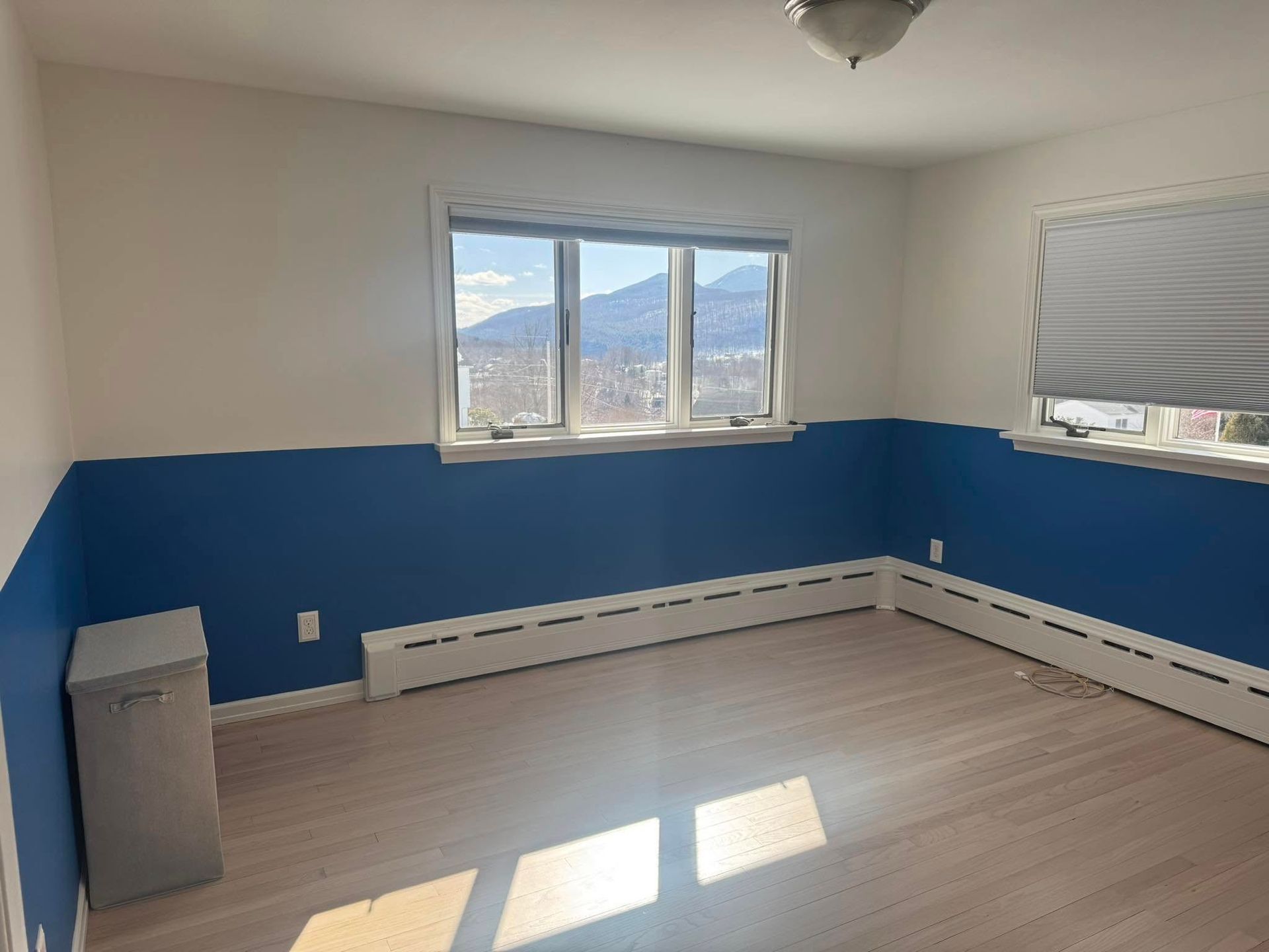 Empty room with blue-and-white walls, window view, and sunlight on the floor
