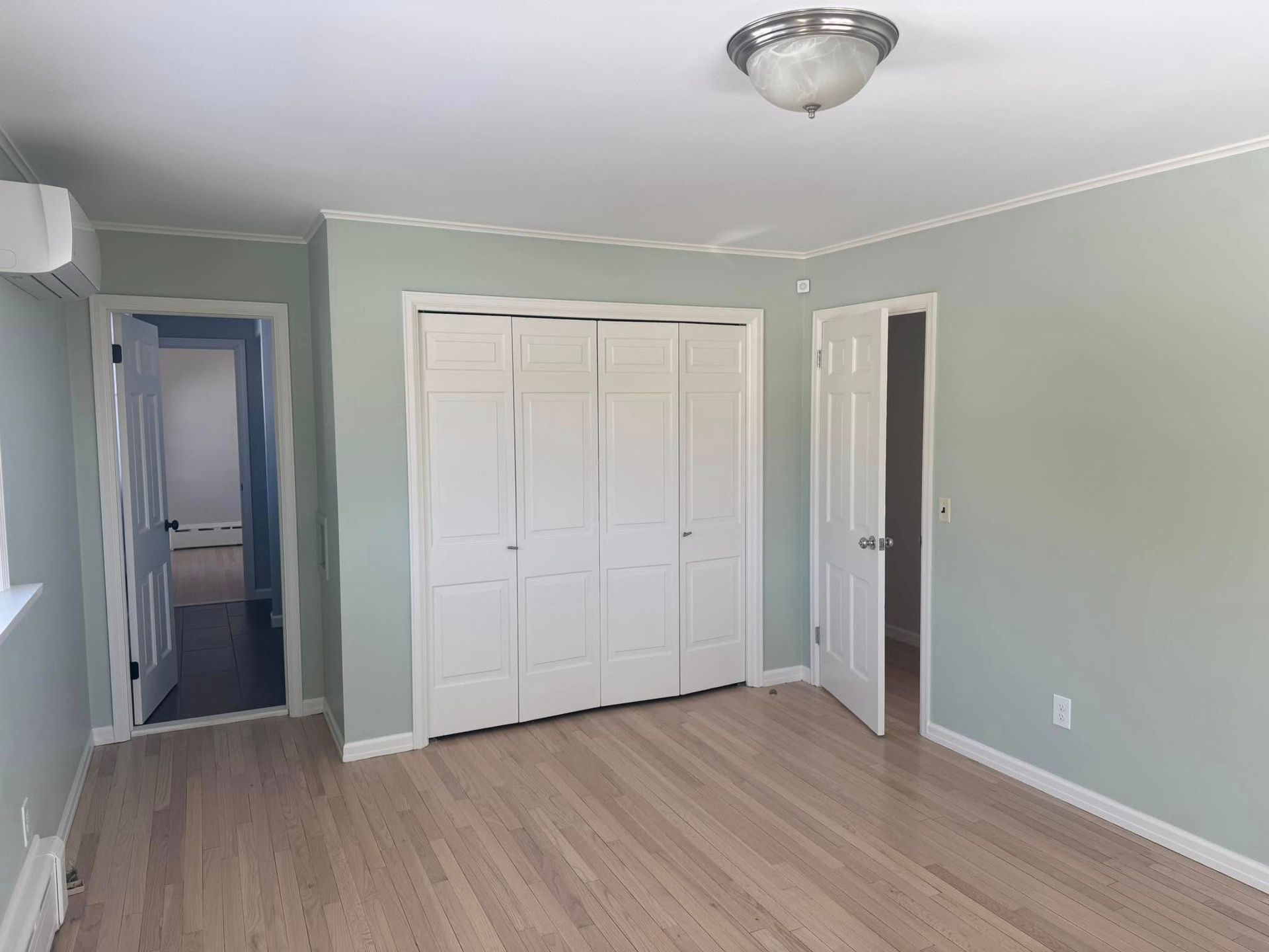 Empty bedroom with light green walls, white closet doors, and wood flooring.