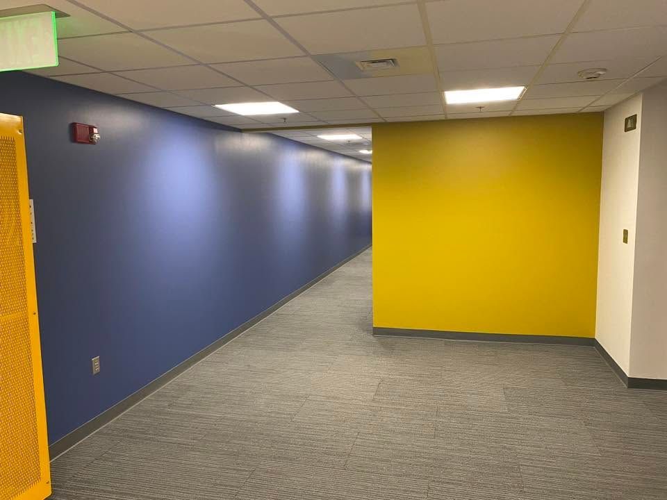 Empty office hallway with blue and yellow walls and gray carpet tiles