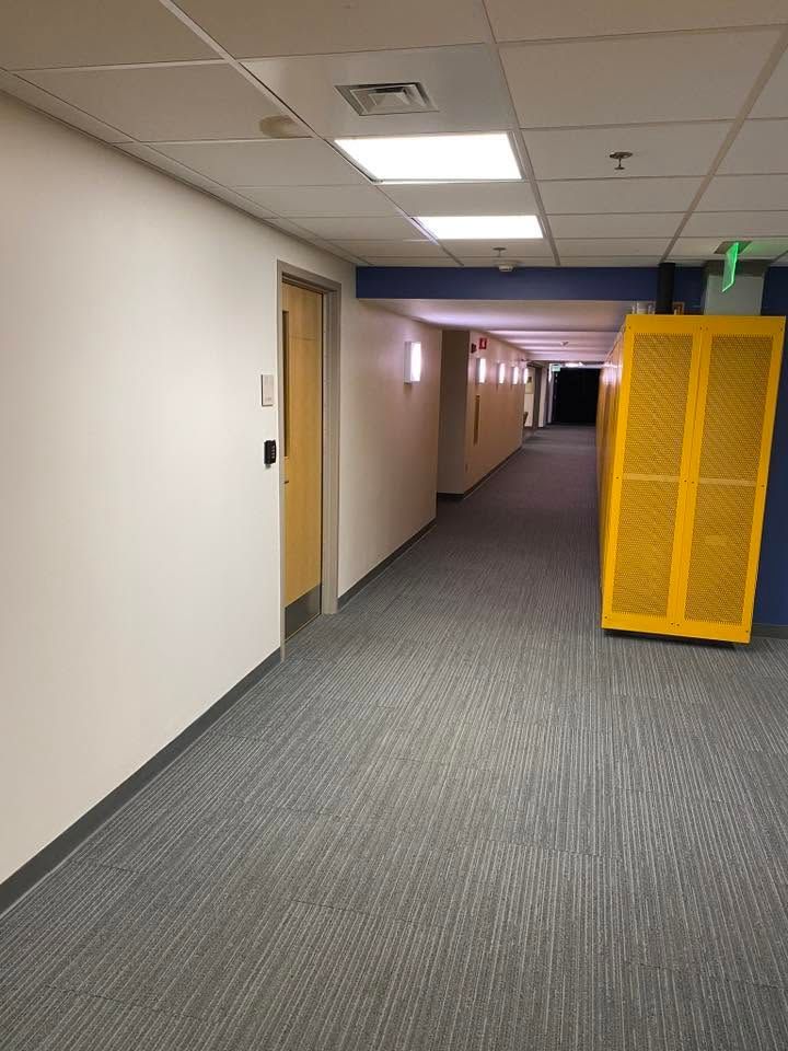 Office hallway with gray carpet, white walls, and a yellow cabinet near the far end