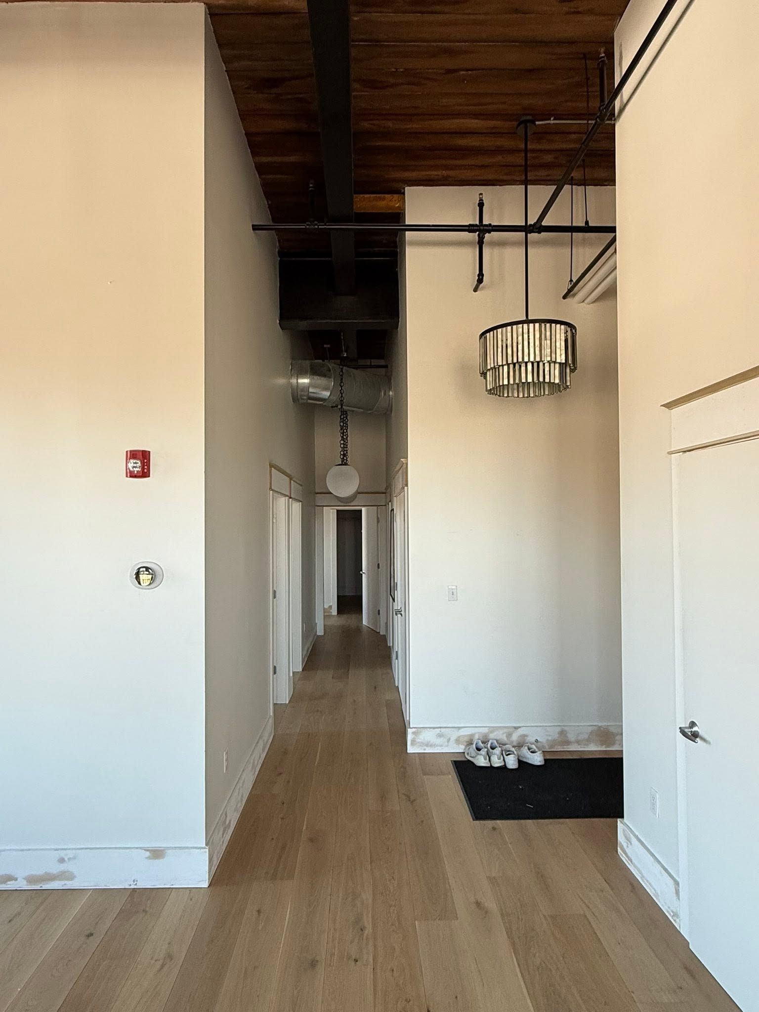 Modern hallway with wood floors, white walls, exposed ceiling, and hanging light fixtures