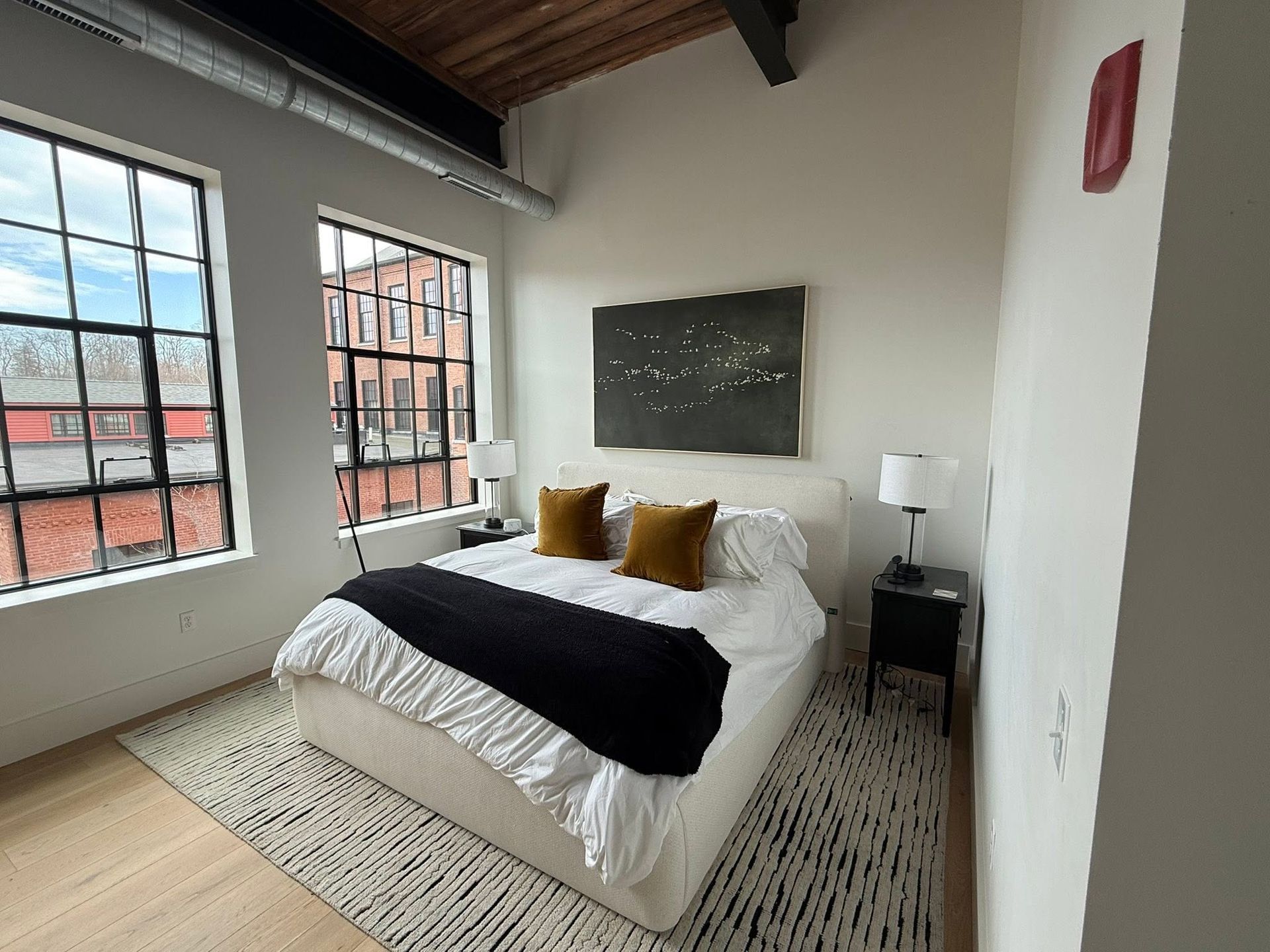 Modern bedroom with large windows, white bedding, black throw, and mustard pillows
