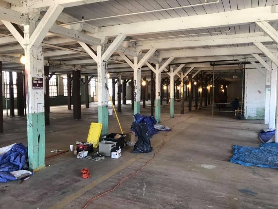 Empty industrial warehouse interior with white beams, scattered tools, and blue tarps on the floor