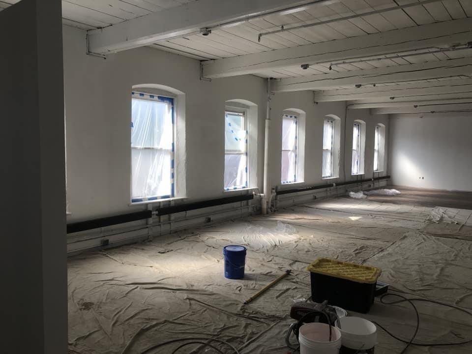 Empty room under renovation with exposed ceiling, covered windows, and construction tools on the floor