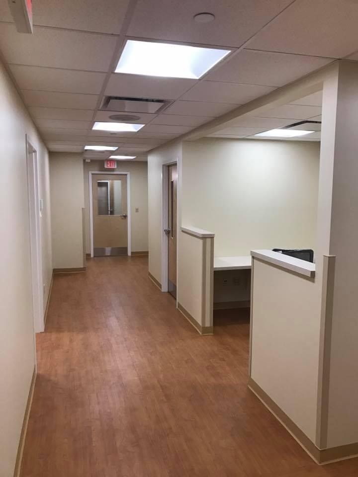 Empty office hallway with wood flooring, beige walls, and fluorescent ceiling lights