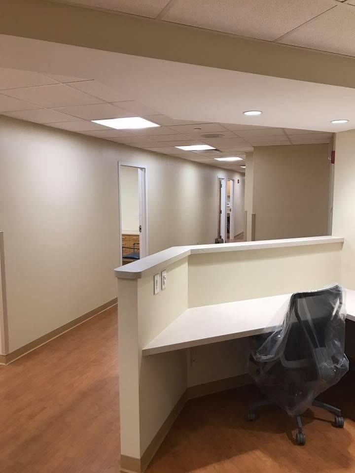 Empty office hallway with beige walls, wood floor, and a desk with a black chair in the foreground