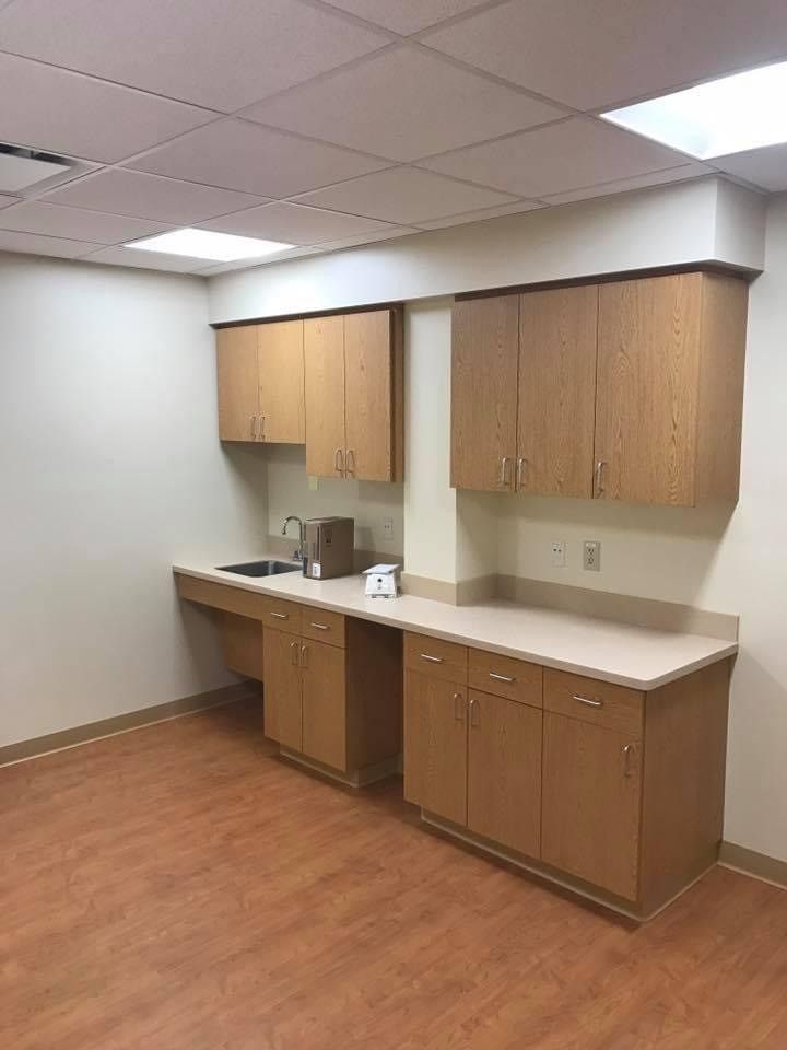 Empty break room with wood cabinets, white countertop, sink, and wood-look floor.