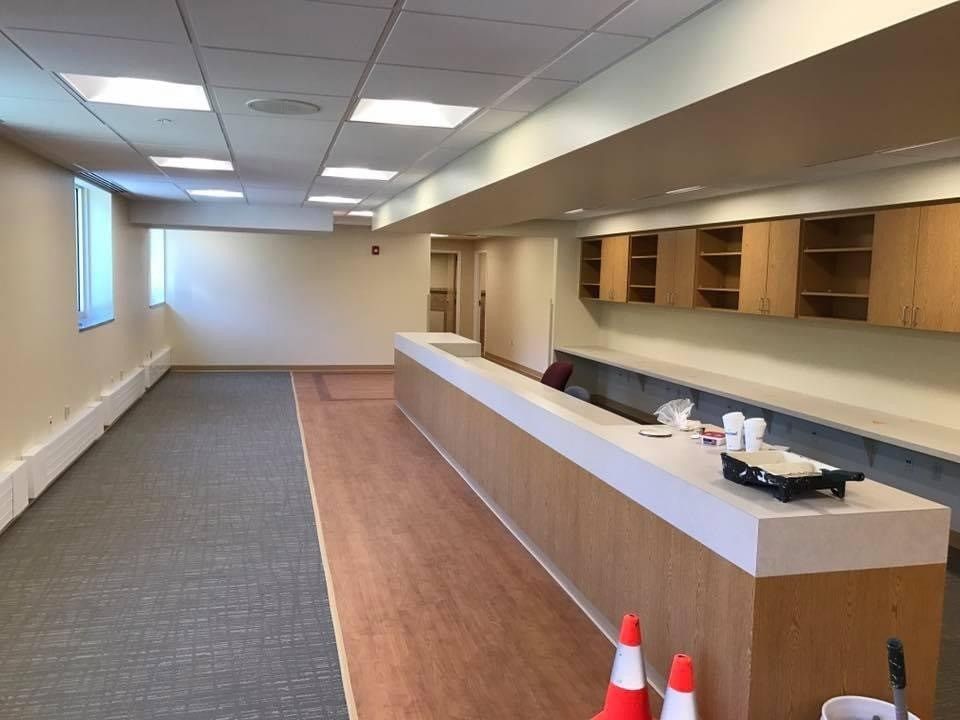 Empty office room with long counter, wooden cabinets, gray carpet, and orange cones near the front
