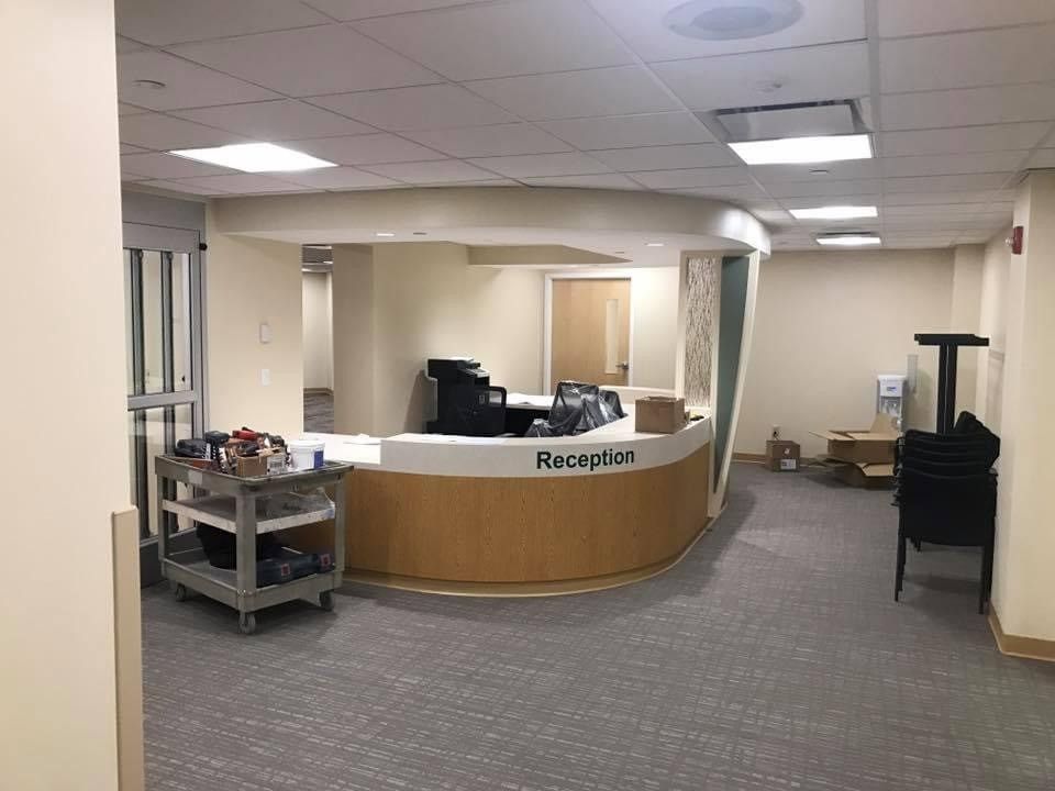 Empty reception desk in a beige office lobby with carpeted floor and overhead fluorescent lights